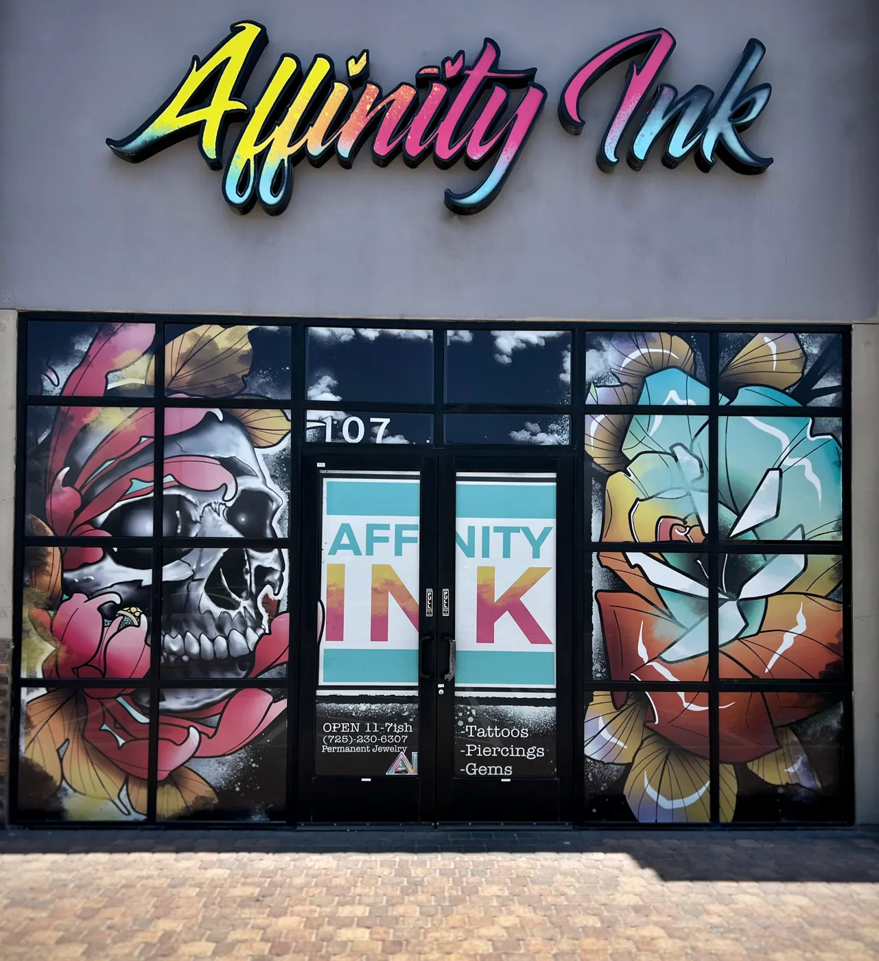 The Affinity Ink storefront at night, neon script sign above windows painted with a skull and roses